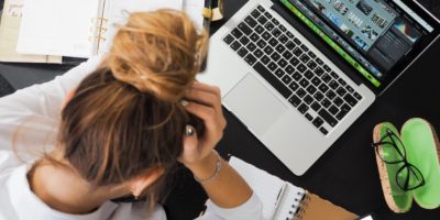 Stressad kvinna sitter vid sin laptop och tar sig på huvudet